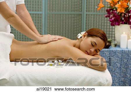 Stock Image - Young woman lying on massage table having back massaged. Fotosearch