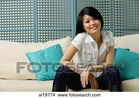 Young woman sitting on sofa, smiling at camera View Large Photo Image Picture - Young woman sitting on sofa, smiling at camera. Fotosearch
