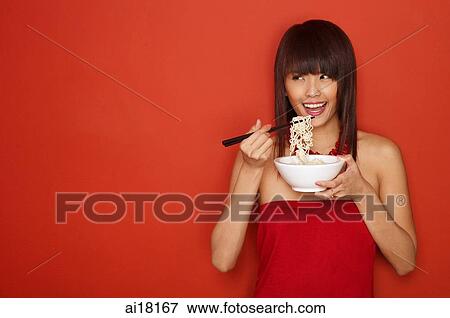 Young woman standing against red wall, eating a bowl of noodles View Large Photo Image Stock Photo - Young woman standing against red wall, eating a bowl of noodles. Fotosearch