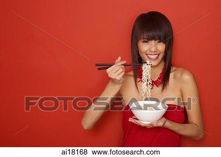 Young woman standing against red wall, holding bowl of noodles, smiling View Large Photo Image Stock Photo - Young woman standing against red wall, holding bowl of noodles, smiling. Fotosearch