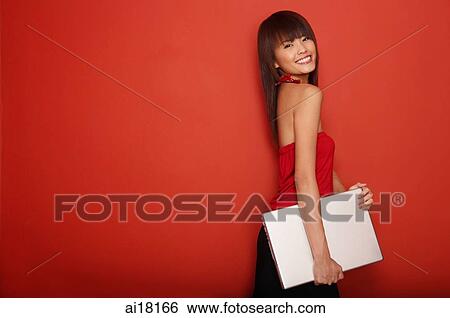 Young woman standing against red wall carrying laptop View Large Photo Image Stock Photograph - Young woman standing against red wall carrying laptop. Fotosearch