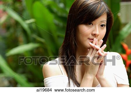 Young woman standing in garden, hands clasped, looking away View Large Photo Image Picture - Young woman standing in garden, hands clasped, looking away. Fotosearch