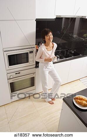 Stock Photo - Young woman standing in kitchen, looking at camera, smiling. Fotosearch