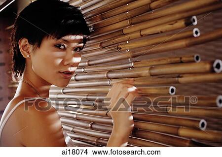 Young woman touching bamboo screen, looking at camera View Large Photo Image Picture - Young woman touching bamboo screen, looking at camera. Fotosearch