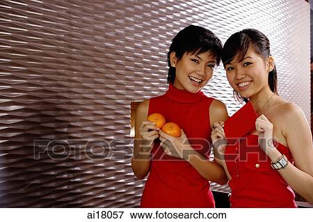 Stock Photo - Young women dressed in red, holding two oranges and red packet. Fotosearch