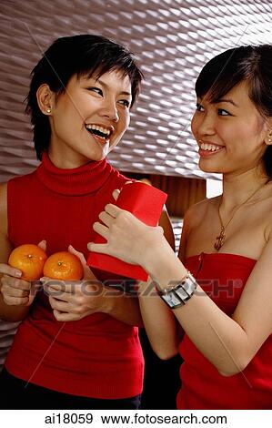 Young women holding two oranges and red packet, smiling at each other View Large Photo Image Stock Photo - Young women holding two oranges and red packet, smiling at each other. Fotosearch