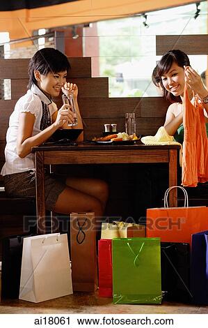 Young women in restaurant, looking at items from shopping bags View Large Photo Image Stock Image - Young women in restaurant, looking at items from shopping bags. Fotosearch