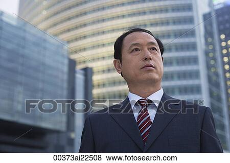 A businessman stands in front of a skyscraper View Large Photo Image Stock Photo - A businessman stands in front of a skyscraper. Fotosearch