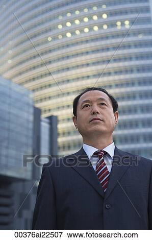 A businessman stands in front of a skyscraper View Large Photo Image Stock Photo - A businessman stands in front of a skyscraper. Fotosearch