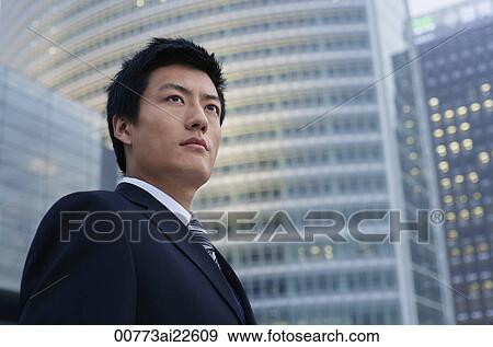 Stock Photo - A businessman stands in front of a skyscraper. Fotosearch