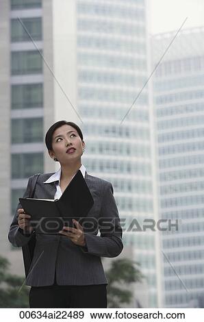 Stock Photo - A businesswoman holds a folder as she stands in the city. Fotosearch