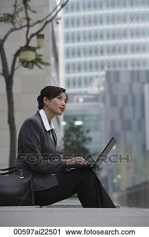 Stock Image - A businesswoman sits down and uses her laptop. Fotosearch