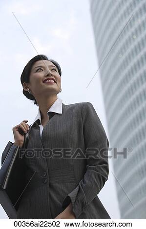 A businesswoman smiles as she stands in front of a skyscraper View Large Photo Image Stock Image - A businesswoman smiles as she stands in front of a skyscraper. Fotosearch