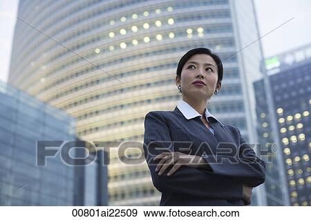 Stock Photo - A businesswoman stands in front of a skyscraper. Fotosearch