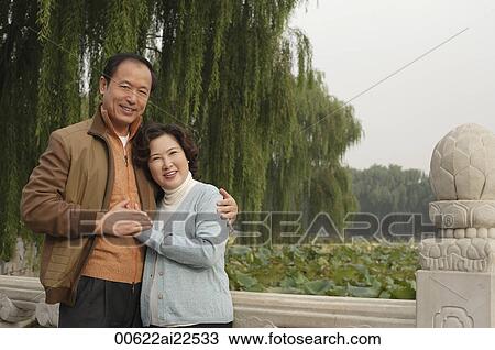 Stock Image - A couple look at the camera with their arms around each other. Fotosearch