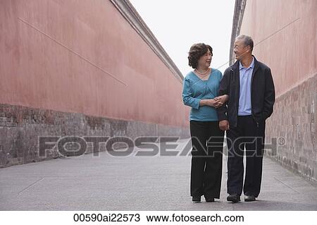 Stock Image - A man and woman link arms as they walk together. Fotosearch