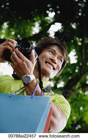 Stock Photo - A man gets ready to take photos as he holds shopping bags. Fotosearch