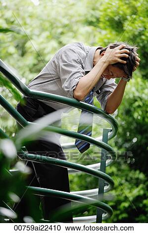 Stock Image - A man looks stressed as he leans on a railing. Fotosearch