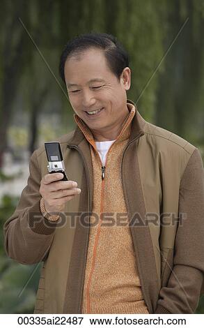 A man uses his cellphone as he stands outdoors View Large Photo Image Stock Photo - A man uses his cellphone as he stands outdoors. Fotosearch