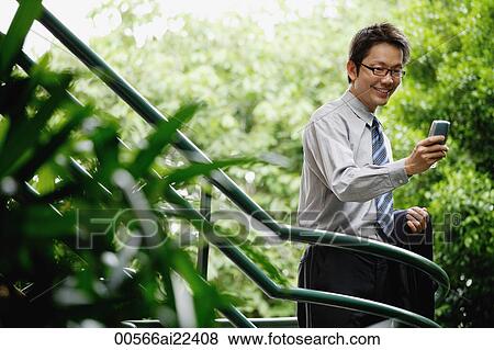 A man uses his cellphone as he stands on stairs surrounded by trees View Large Photo Image Stock Photo - A man uses his cellphone as he stands on stairs surrounded by trees. Fotosearch