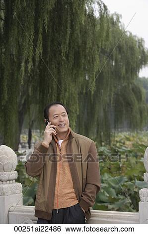 A man uses his cellphone as he stands outdoors View Large Photo Image Stock Photograph - A man uses his cellphone as he stands outdoors. Fotosearch