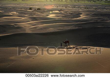 Stock Photograph - A tourist riding on camel back in the dune, Shanshan, Turpan, Xinjiang. Fotosearch