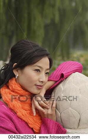 Picture - A woman looks into the distance as she leans on a stone wall. Fotosearch