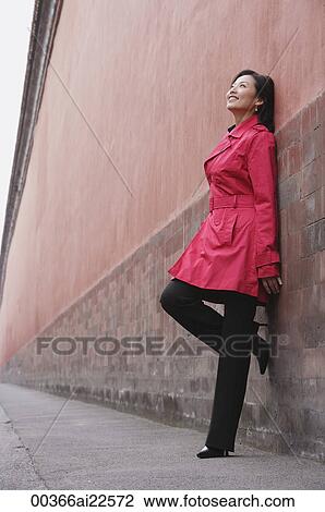 A woman smiles as she leans against a wall View Large Photo Image Stock Image - A woman smiles as she leans against a wall. Fotosearch