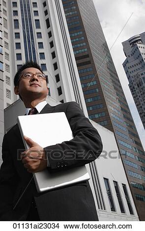 Picture - Businessman holding laptop and looking into distance. Fotosearch