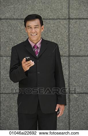 Stock Image - Businessman holding phone, looking at camera. Fotosearch