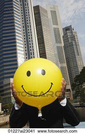 Stock Image - Businessman holding up smiley face balloon. Fotosearch