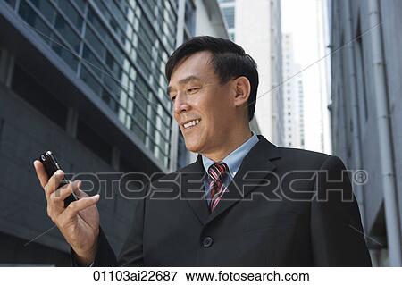 Businessman looking at mobile phone, smiling View Large Photo Image Stock Photo - Businessman looking at mobile phone, smiling. Fotosearch