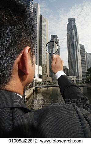 Businessman looking through magnifying glass at skyscrapers View Large Photo Image Stock Image - Businessman looking through magnifying glass at skyscrapers. Fotosearch