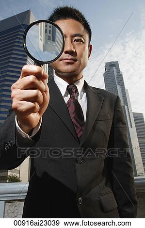 Stock Photo - Businessman looking through magnifying glass at camera. Fotosearch
