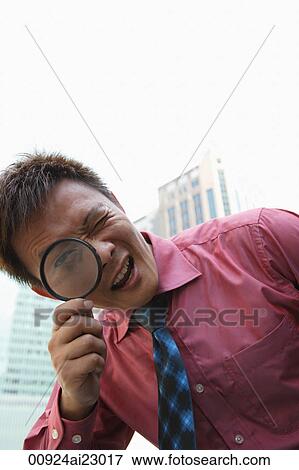 Stock Photo - Businessman looking through magnifying glass at camera. Fotosearch
