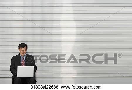 Stock Photo - Businessman sits outdoor with laptop on his lap. Fotosearch