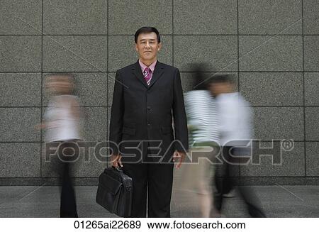 Stock Photo - Businessman standing in crowd, looking at camera. Fotosearch