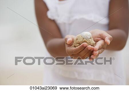 Stock Photo - Close-up of girl holding sand with shell. Fotosearch