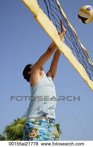 Stock Photo - Guy playing volleyball, hitting ball over net. Fotosearch