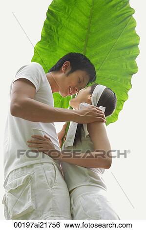 Stock Photograph - Man and woman kissing under large leaf. Fotosearch