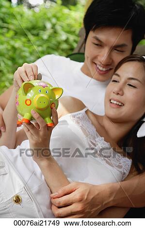 Man and woman lounging on chair and putting money in piggy bank View Large Photo Image Stock Photo - Man and woman lounging on chair and putting money in piggy bank. Fotosearch