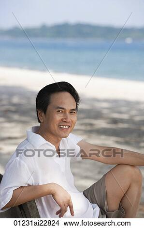 Man at the beach sitting on a bench, looking at camera View Large Photo Image Picture - Man at the beach sitting on a bench, looking at camera. Fotosearch