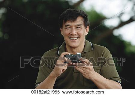 Stock Photography - Man holding camera, taking picture, smiling. Fotosearch