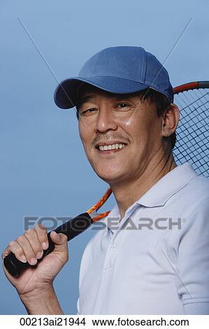 Picture - Man holding tennis racket over shoulder, smiling at camera. Fotosearch