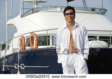 Stock Image - Man in front of yacht, smiling at camera. Fotosearch