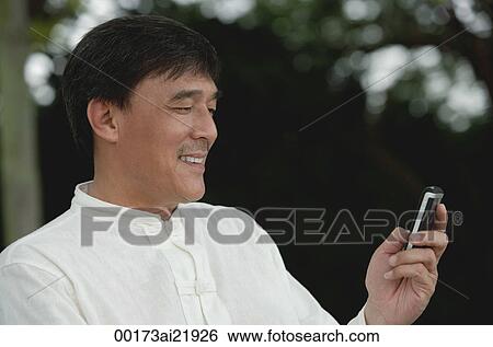 Stock Photograph - Man in park sending, reading text message on mobile phone. Fotosearch