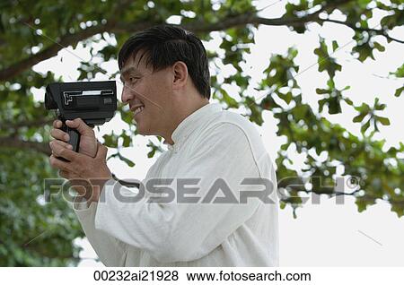 Stock Photo - Man in park using super 8 movie camera. Fotosearch