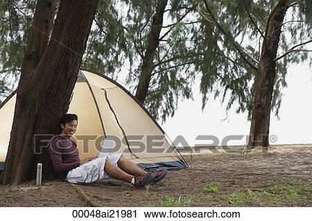 Man leaning against tree holding laptop, camping on beach View Large Photo Image Stock Image - Man leaning against tree holding laptop, camping on beach. Fotosearch