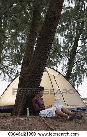 Man leaning against tree working on laptop, camping View Large Photo Image Stock Image - Man leaning against tree working on laptop, camping. Fotosearch