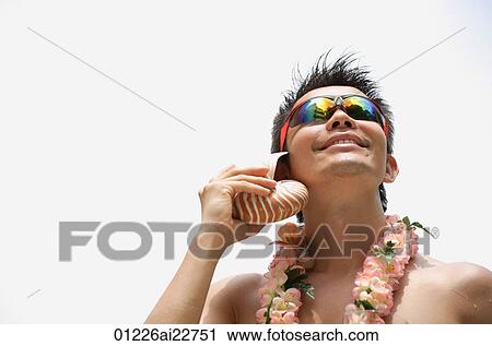 Stock Image - Man listening to sea shell. Fotosearch